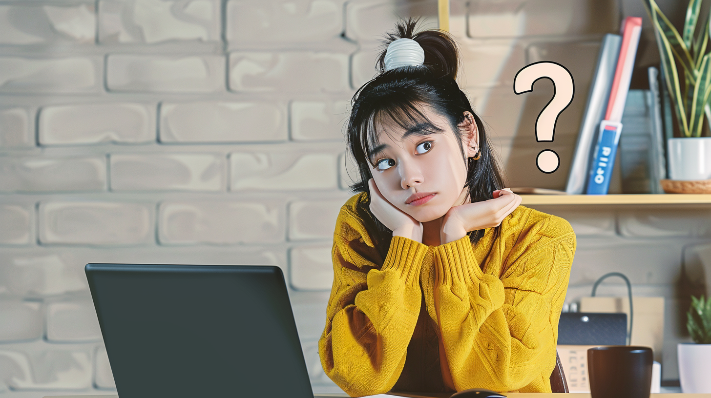 困った表情でノートパソコンを見つめる黄色いセーターを着た日本人女性